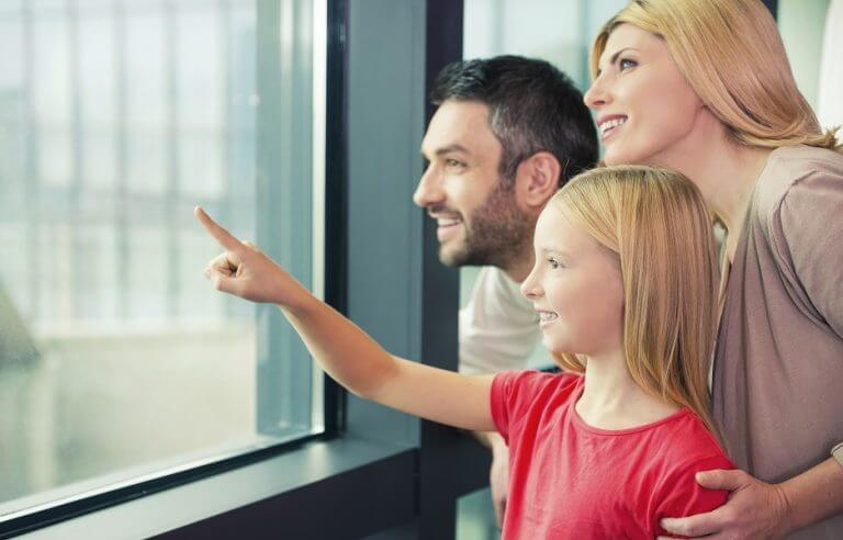Is it a plane? Happy family of three bonding to each other and smiling while looking through a window together